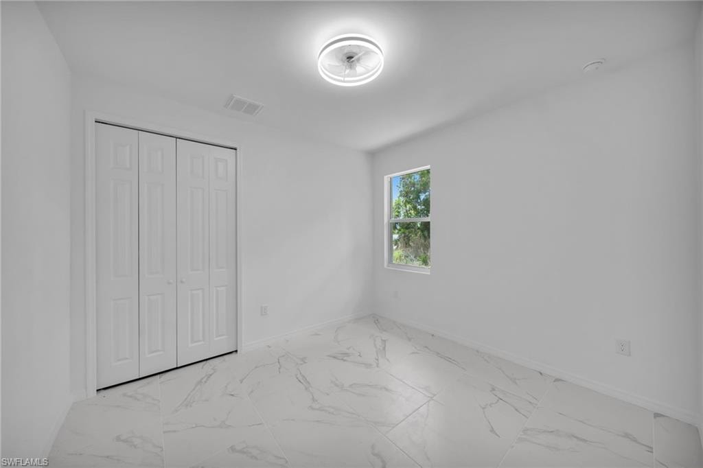 GUEST BEDROOM 1 Room featuring white walls, large format tile flooring, a single window, and bi-fold closet doors