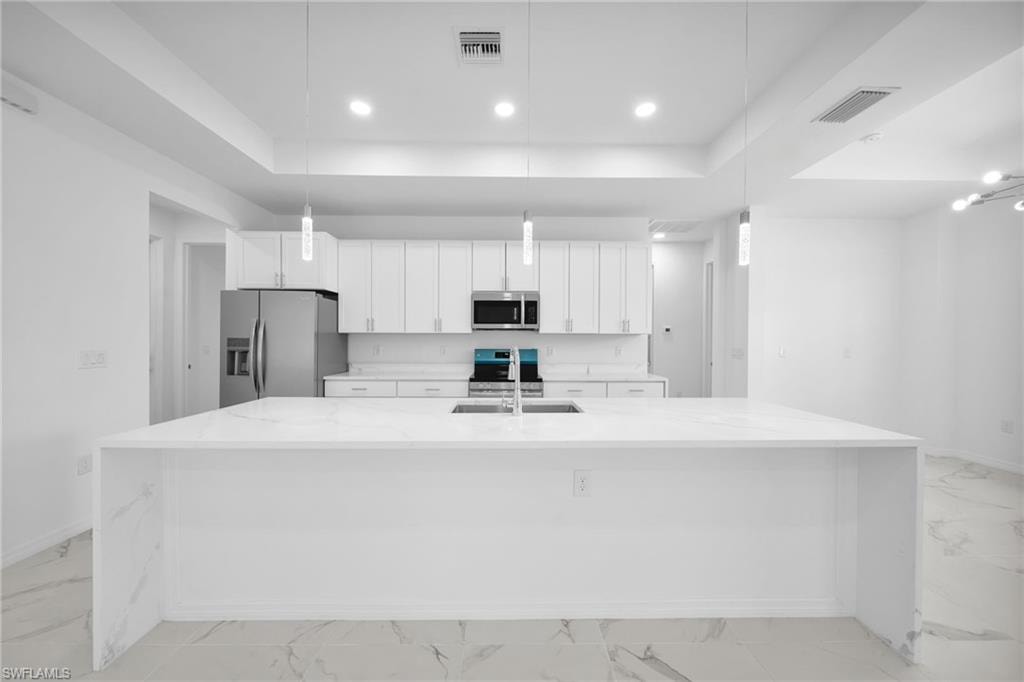 Spacious kitchen featuring a large waterfall-edge island with white countertops, white shaker cabinetry, stainless steel appliances, and pendant lighting