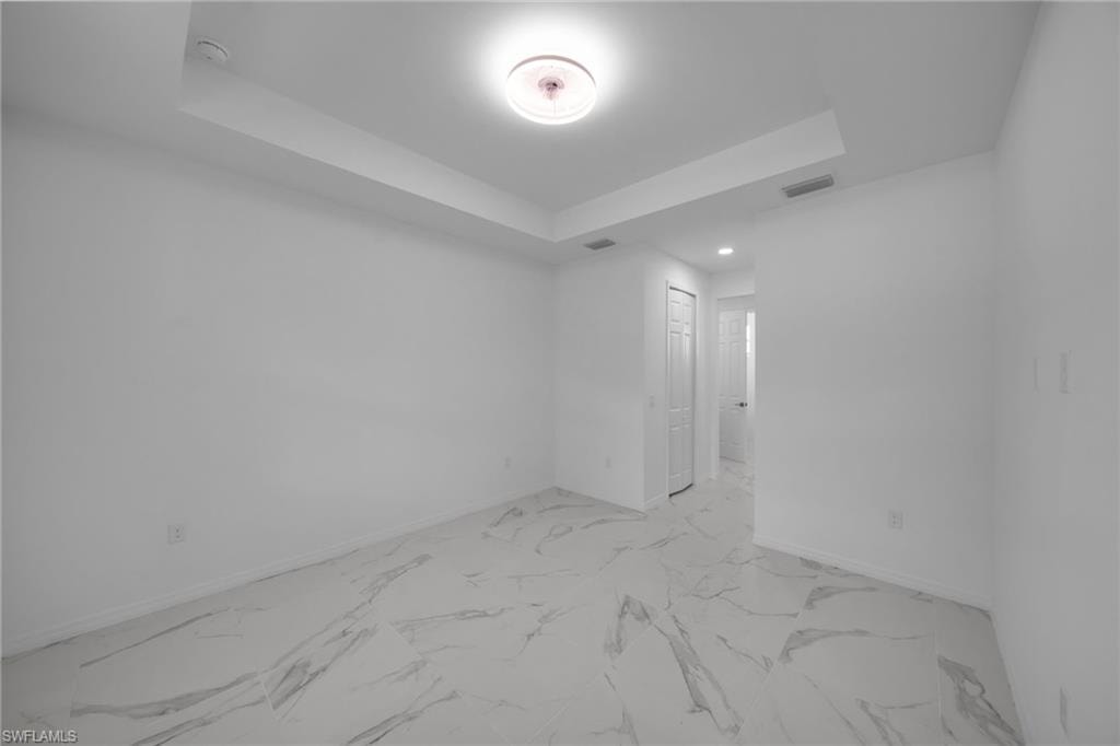MASTER Spacious room featuring large format tile flooring with distinctive veining, a tray ceiling, and a flush mount ceiling fixture