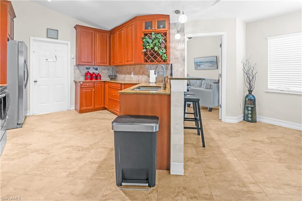 Kitchen featuring wood cabinetry, stone tile flooring, stainless steel appliances, a corner sink with a high-arch faucet, and a breakfast bar