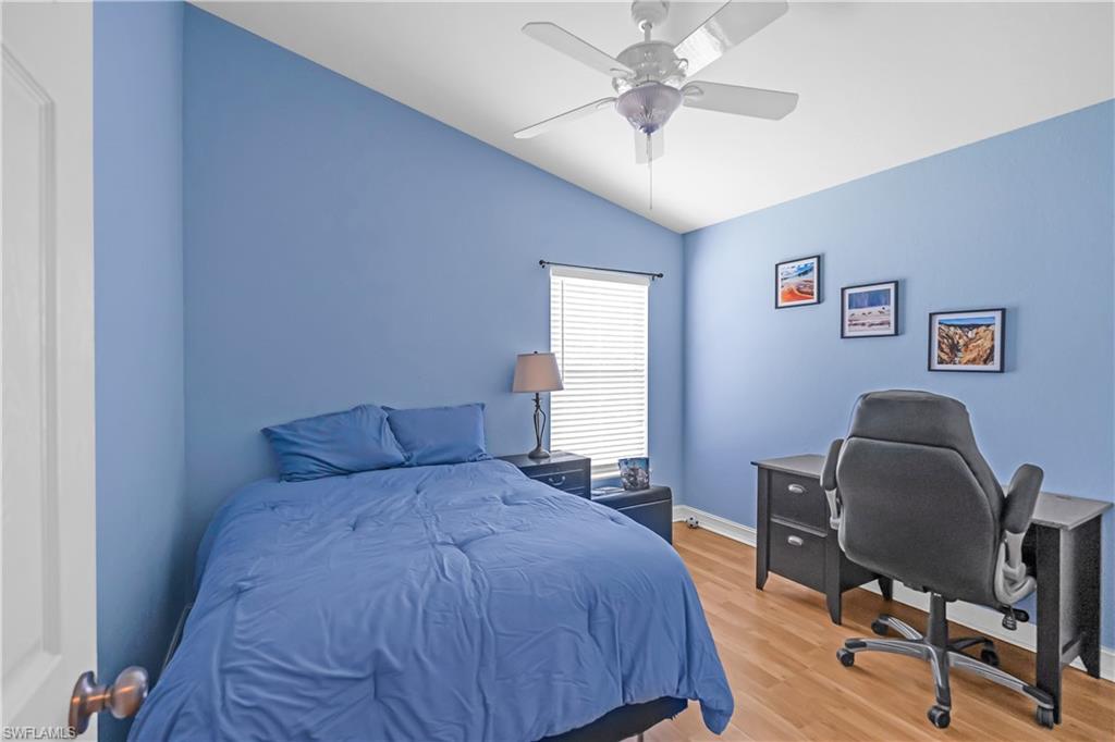 Vaulted ceiling with a ceiling fan, window with horizontal blinds, and wood-finish flooring