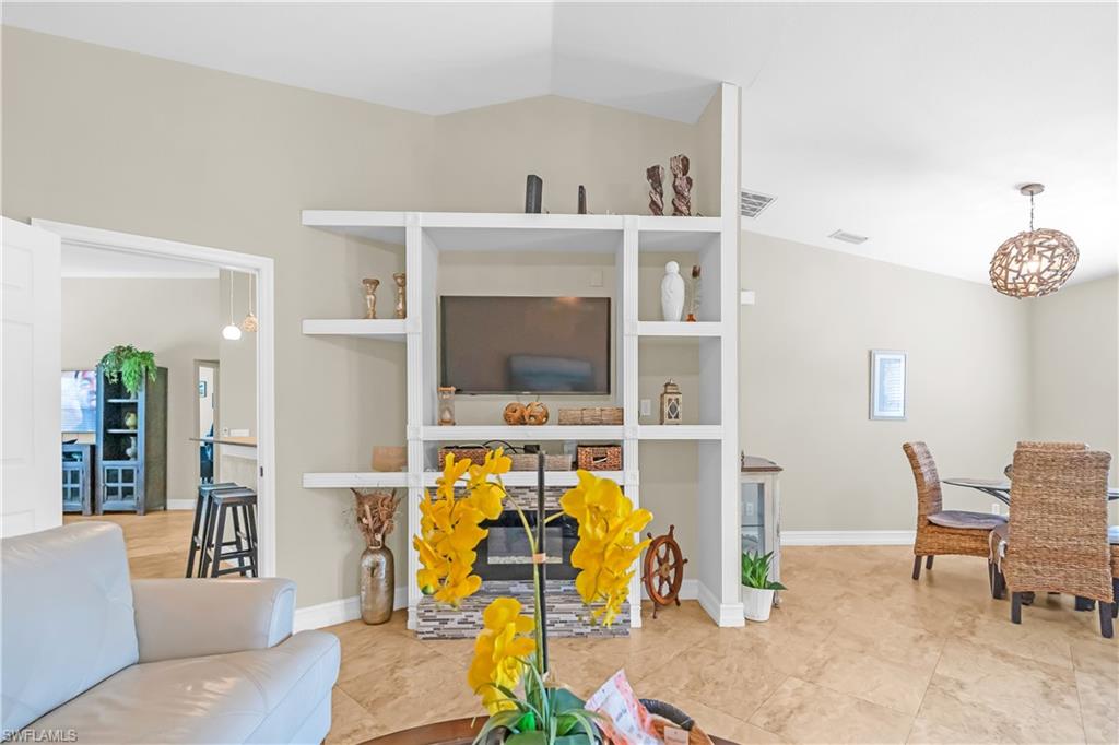 Vaulted ceiling with an open floor plan, featuring built-in shelving, a tiled fireplace surround, and tile flooring