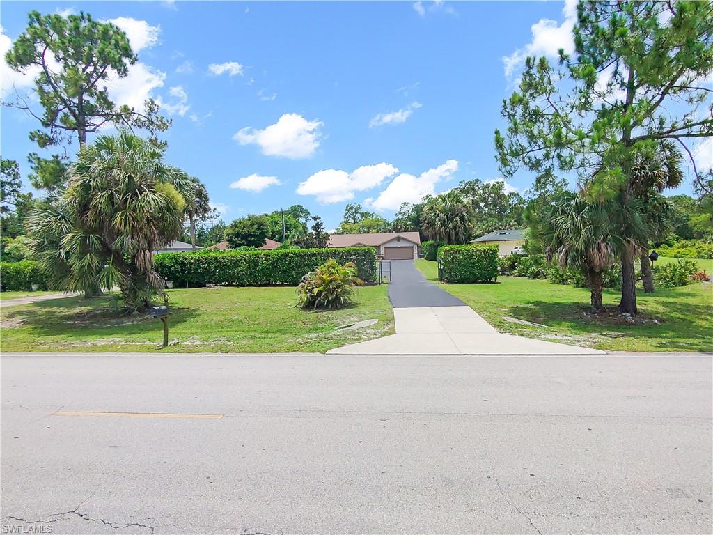 Paved driveway with a two-car garage, mature landscaping, and an expansive front lawn