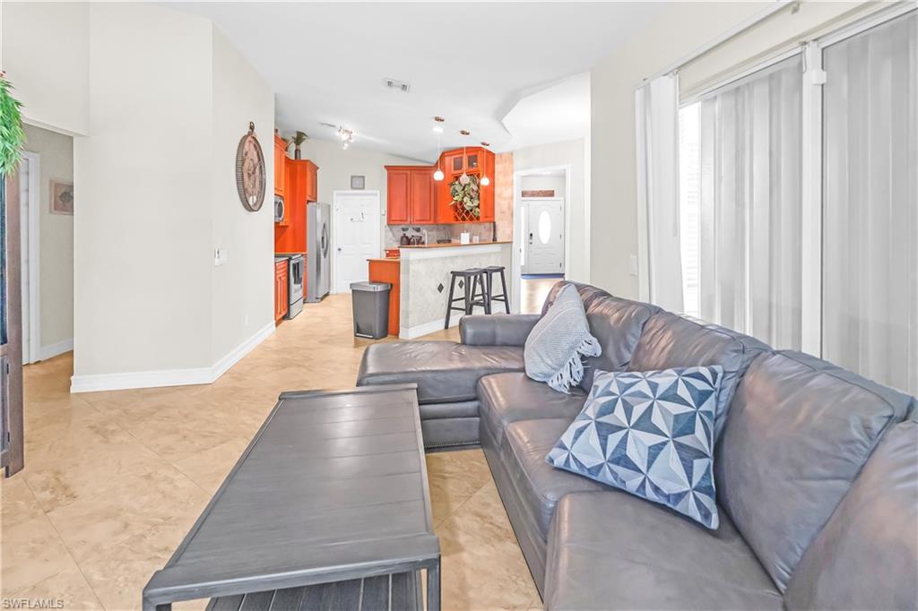 Open-concept living space with tile flooring, a vaulted ceiling, and access to a kitchen with wood cabinetry and stainless steel appliances