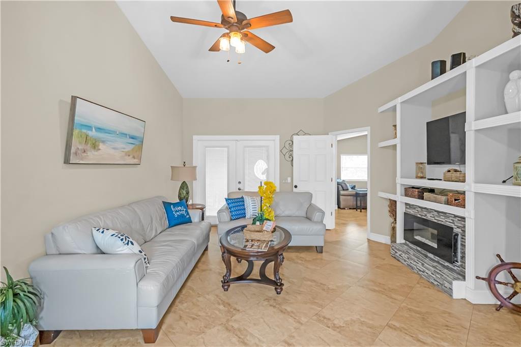 Vaulted ceiling with a ceiling fan, tile flooring, built-in shelving with an electric fireplace, and white paneled doors