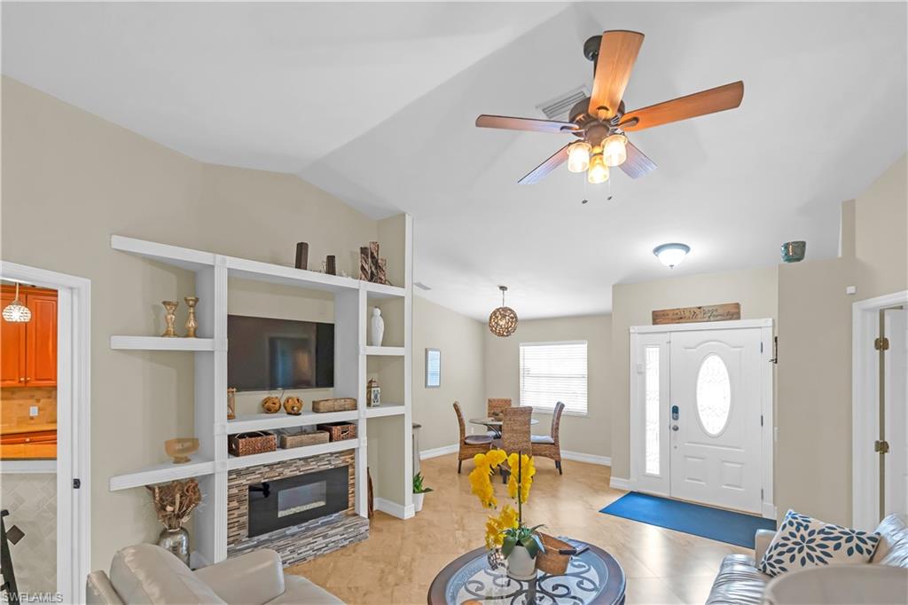Vaulted ceilings, wood-finish flooring, built-in entertainment center with stone-clad fireplace, ceiling fan with light fixture, and double entry doors