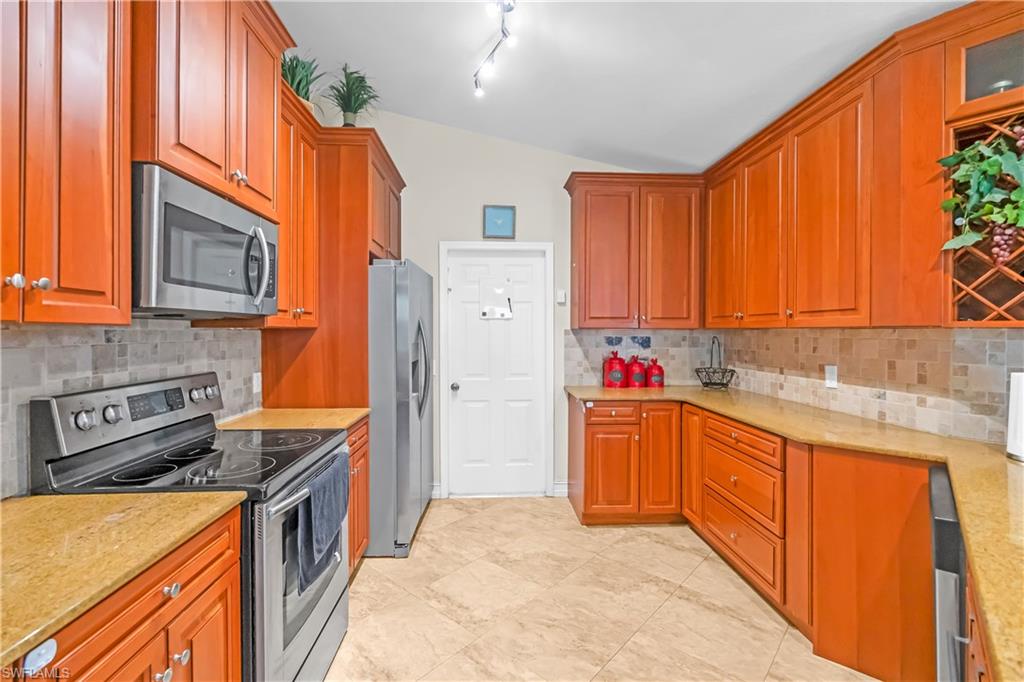 Kitchen featuring wood cabinetry, stainless steel appliances, tile flooring, stone countertops, and a tile backsplash