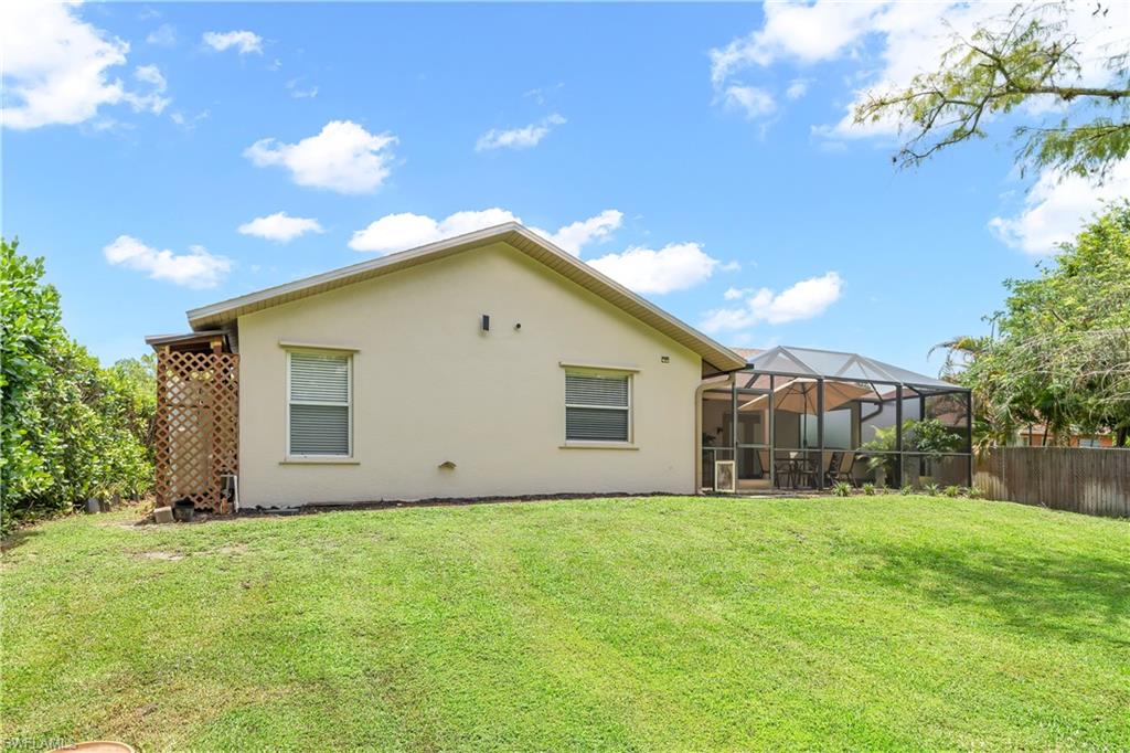 Expansive backyard with a manicured lawn, stucco exterior, screened patio enclosure, and a wood lattice privacy screen