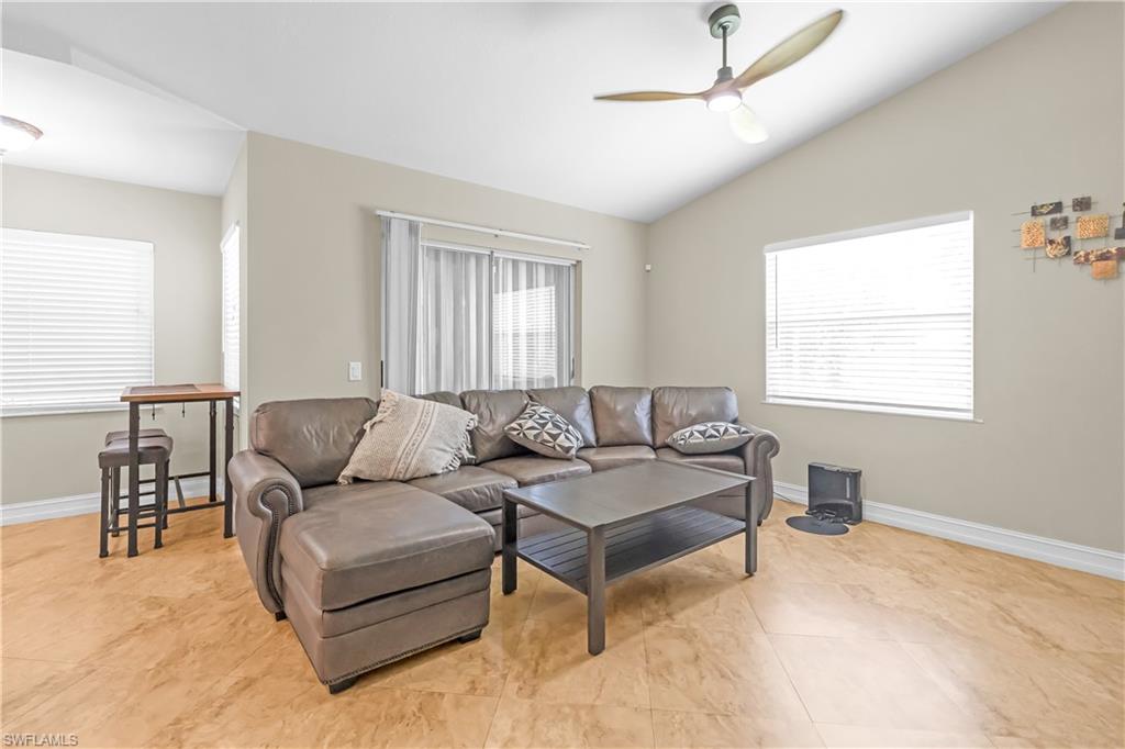 Vaulted ceiling, ceiling fan with integrated lighting, wood-finish flooring, multiple windows, sliding glass door with sheer curtains