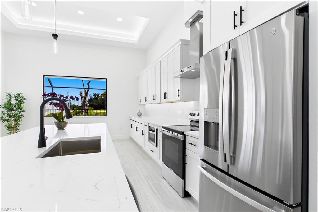 CHEF’S KITCHEN showcases expansive QUARTZ SURFACES, floor-to-ceiling WHITE SHAKER CABINETRY, matte-black fixtures & stainless-steel appliances beneath a dramatic LED-LIT TRAY CEILING.