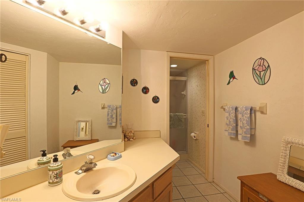 Bathroom featuring a single vanity with an integrated sink, full-width mirror, overhead vanity lighting, and tile flooring