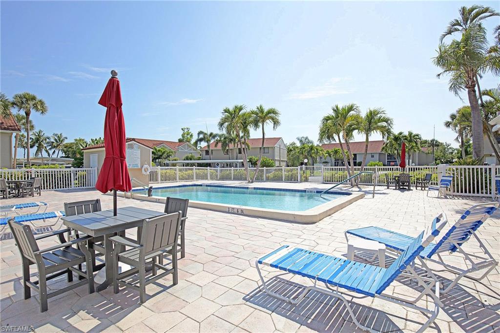Swimming pool with a paved deck, surrounded by palm trees and a white picket fence