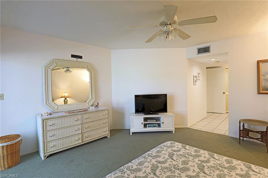 Spacious master bedroom featuring neutral carpeting, a ceiling fan with integrated lighting, and an ensuite dressing area with mirrored vanity and multi-drawer storage