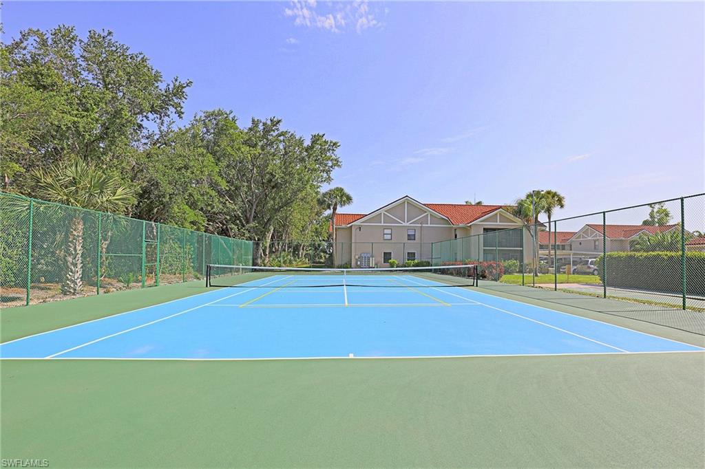 Outdoor tennis court with a blue playing surface and green surrounds, enclosed by chain-link fencing