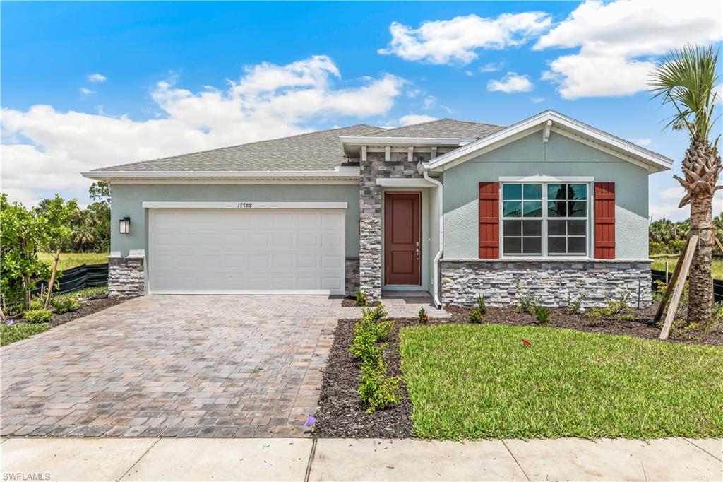 Stucco exterior with stone veneer accents, paver driveway, single-panel garage door, and a red front door