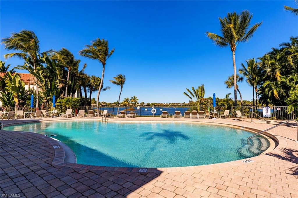 Oval-shaped swimming pool with integrated steps, surrounded by a paved deck, tropical landscaping, and water frontage