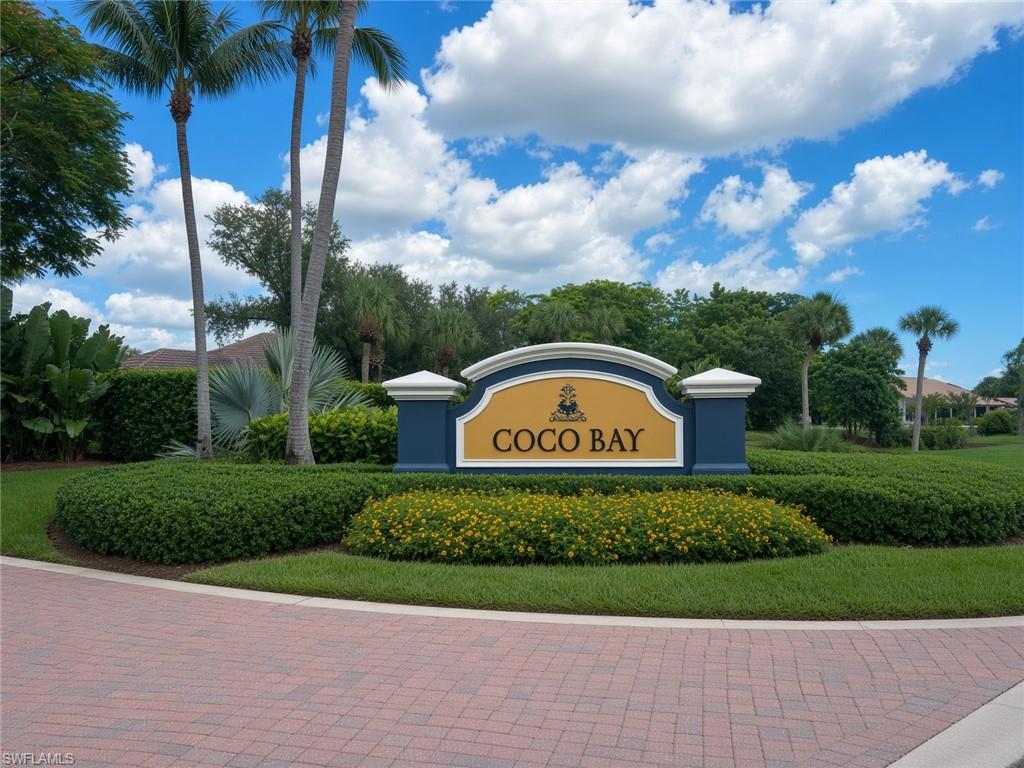 Entry to Coco Bay with established tropical landscaping, mature palm trees, vibrant floral plantings, and brick paver entrance