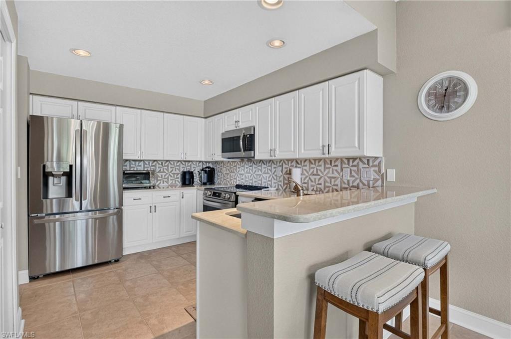 Kitchen featuring white cabinetry, stainless steel appliances, a patterned tile backsplash, recessed lighting, and a breakfast bar with a light-toned countertop