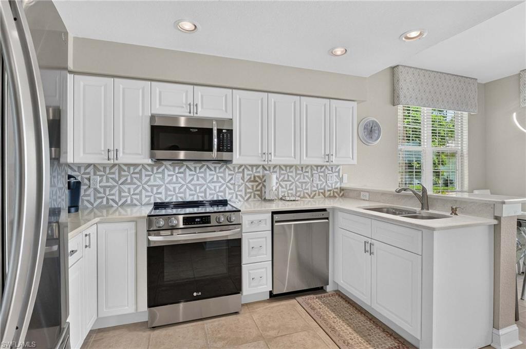 White cabinetry with stainless steel appliances, patterned tile backsplash, light-toned countertops, and recessed lighting