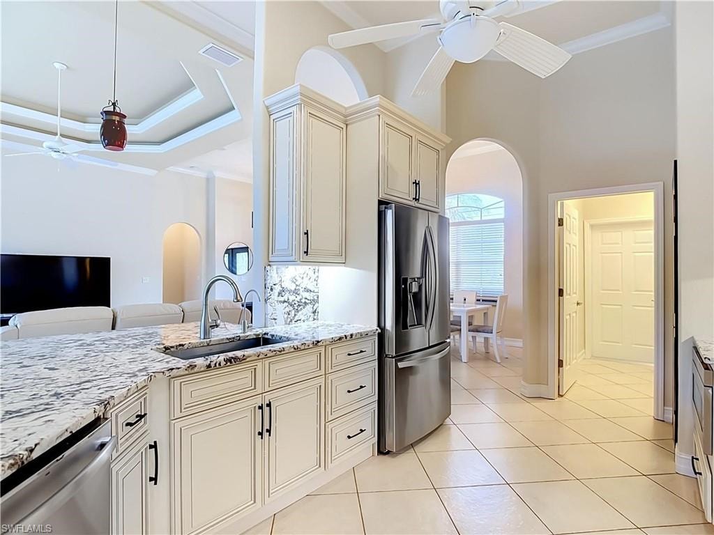 Kitchen featuring cream cabinetry, stainless steel appliances, a large island with a sink, and light-toned tile flooring