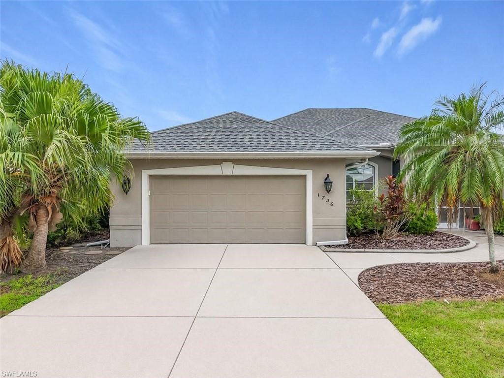 Concrete driveway, attached garage, exterior wall lantern, front landscaping, and an arched window