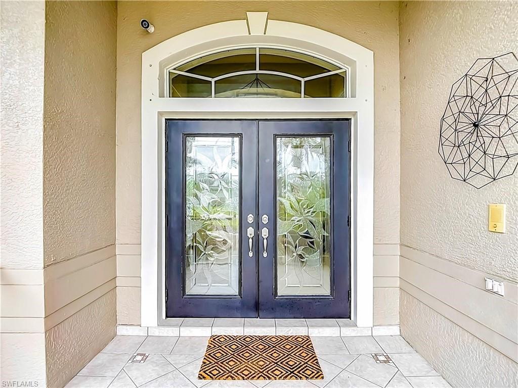 Double entry doors with decorative glass panels and an arched transom window, set within a stucco facade and tile flooring