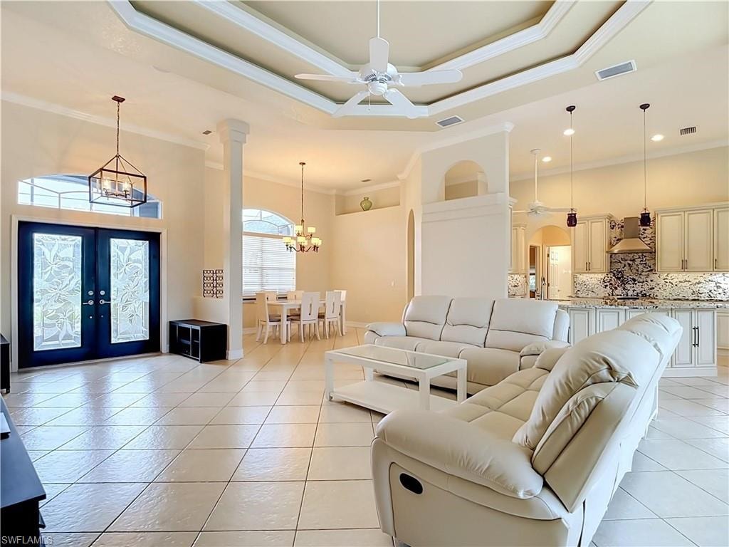Tray ceiling with crown molding, double entry doors with decorative glass inserts, tile flooring, pendant lighting, and recessed kitchen cabinetry