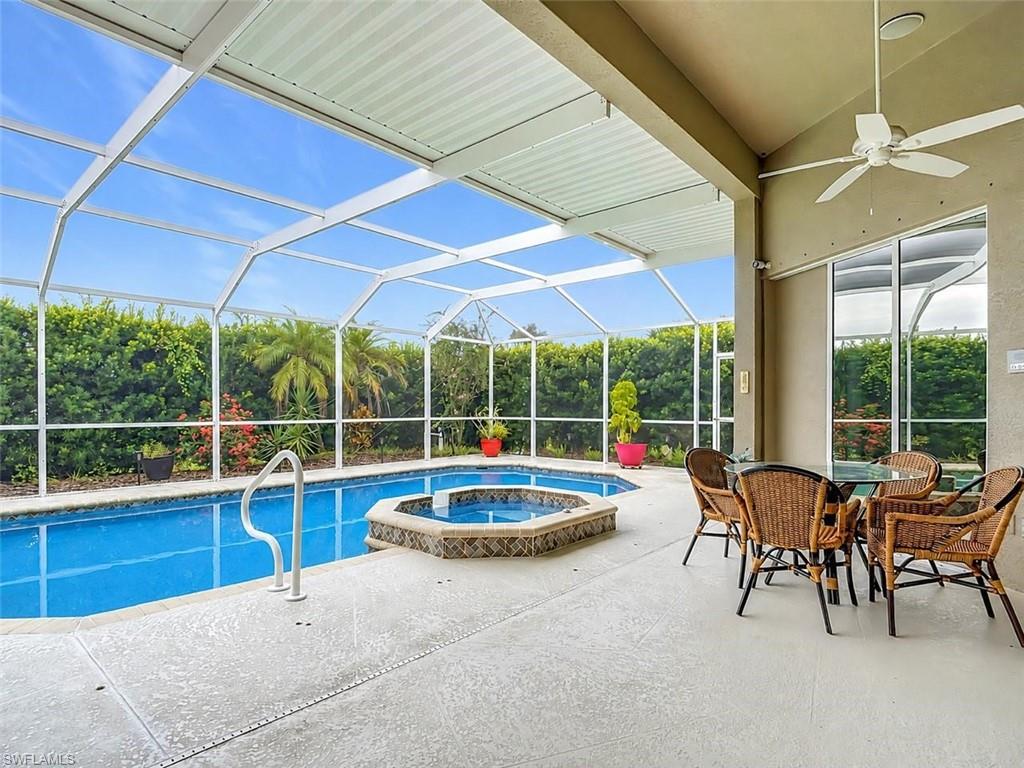 Screened-in swimming pool and spa with a concrete deck, covered patio, and ceiling fan