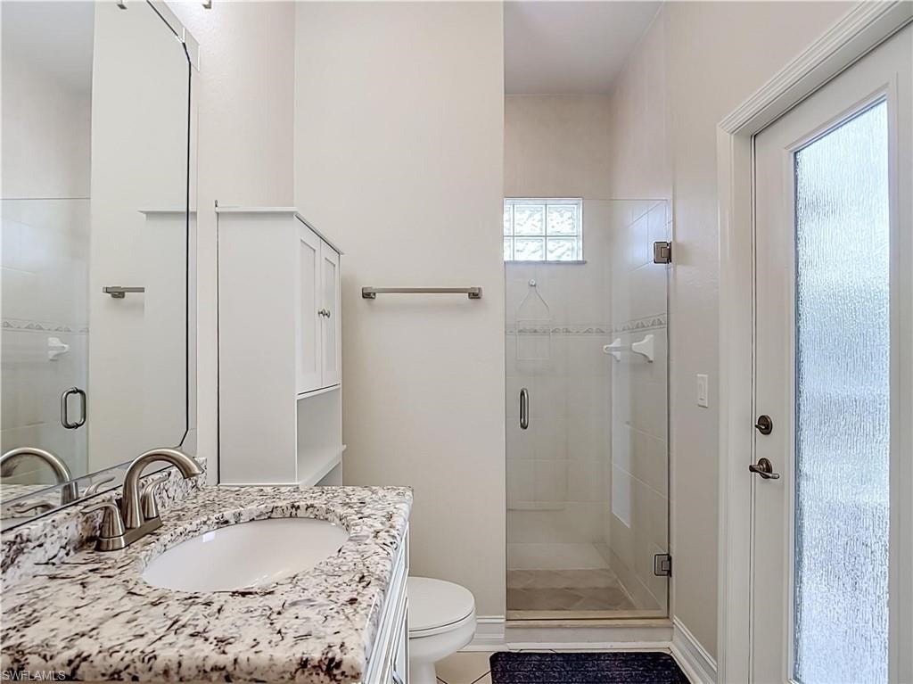 Vanity with stone countertop and undermount sink, brushed nickel faucet, glass-enclosed shower, white wall-mounted cabinet, and frosted glass door