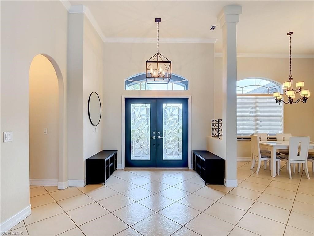 Grand foyer featuring dual blue-painted entry doors with transom windows, white columns, tile flooring, pendant lighting, and archways leading to adjoining spaces