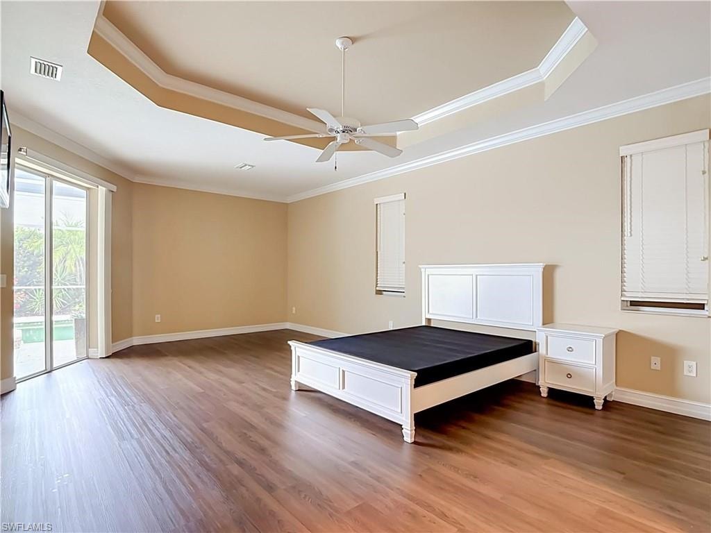 Recessed tray ceiling with crown molding, wood-finish flooring, ceiling fan, and sliding glass door to exterior