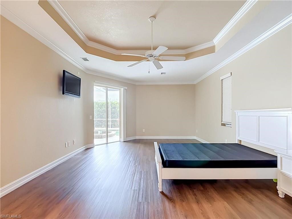 Tray ceiling with crown molding, wood-finish flooring, ceiling fan, and sliding glass door