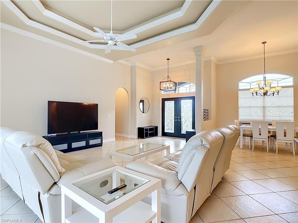 Tray ceiling with crown molding, ceiling fan, arched doorways, tiled flooring, and a decorative double entry door