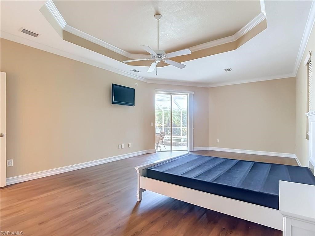 Tray ceiling with crown molding, ceiling fan, wood-finish flooring, and sliding glass door