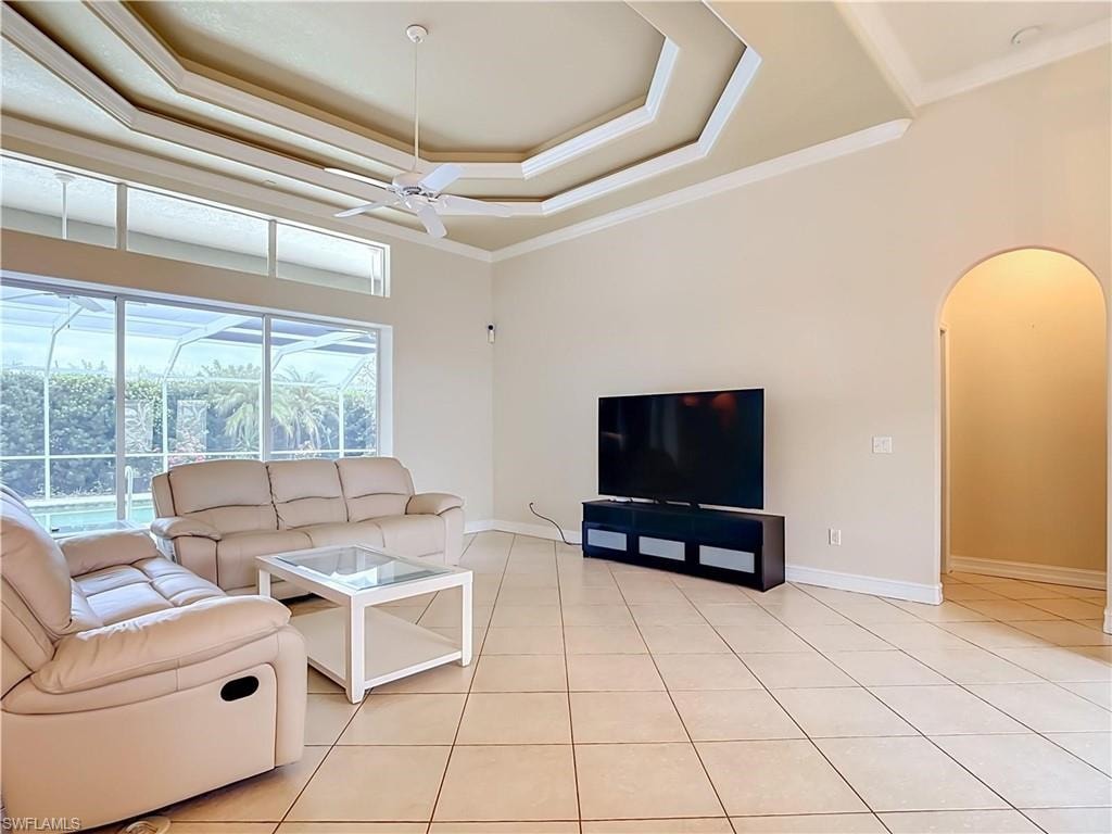 Tray ceiling with crown molding, tiled flooring, large windows, transom windows, and an arched doorway