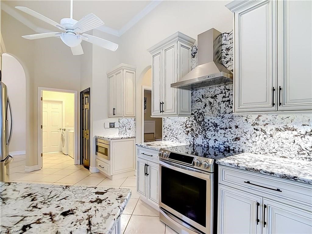 Vaulted ceiling with crown molding, white shaker-style cabinetry, stainless steel range hood, built-in microwave, and patterned stone countertops with matching backsplash