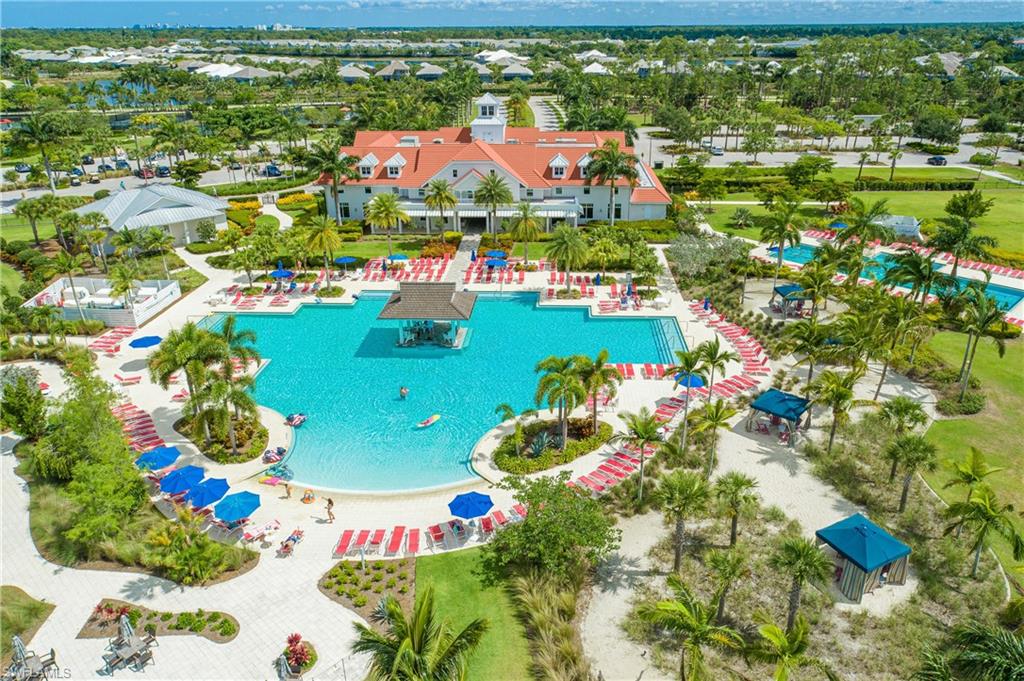 Resort-style pool area featuring multiple swimming pools, extensive lounge seating, a swim-up bar, and surrounding mature palm trees