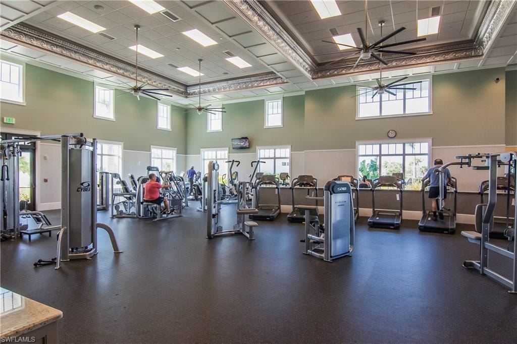 Spacious fitness center featuring high ceilings, decorative ceiling molding, multiple windows, large ceiling fans, and various exercise machines