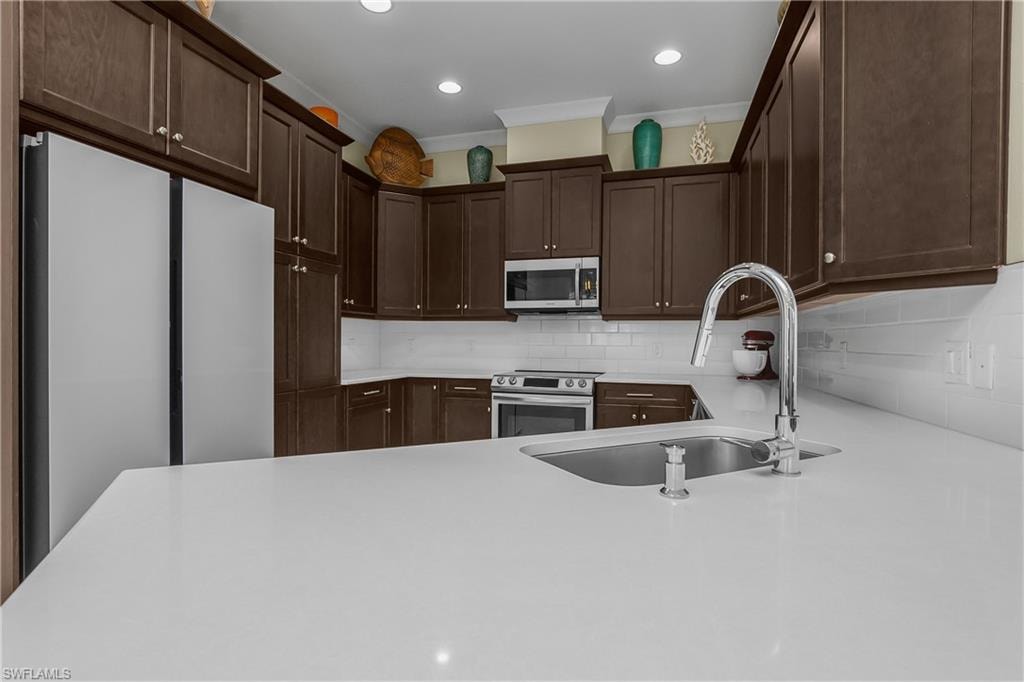 U-shaped kitchen featuring wood-finish cabinetry, stainless steel appliances, white subway tile backsplash, and light-colored countertops