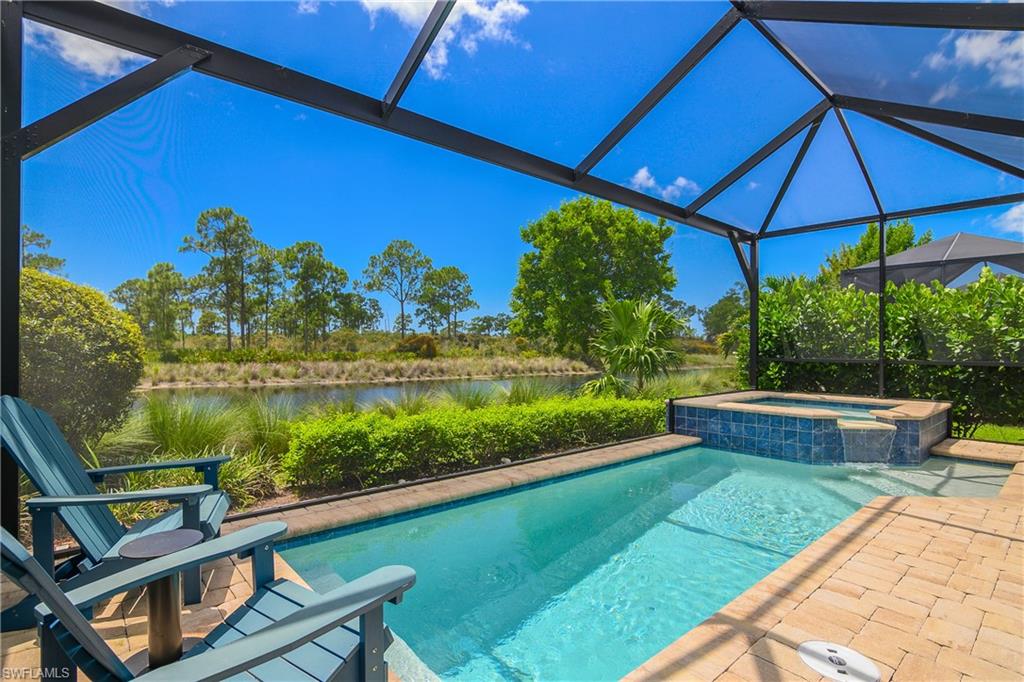 Screened outdoor living area featuring a rectangular pool, integrated spa with waterfall, and a paver deck