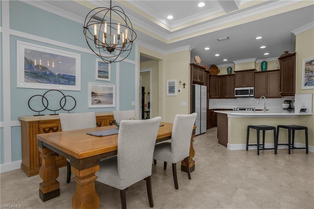 Tray ceiling with recessed lighting, pendant lighting fixture, wood-finish cabinetry, stainless steel appliances, and tile flooring