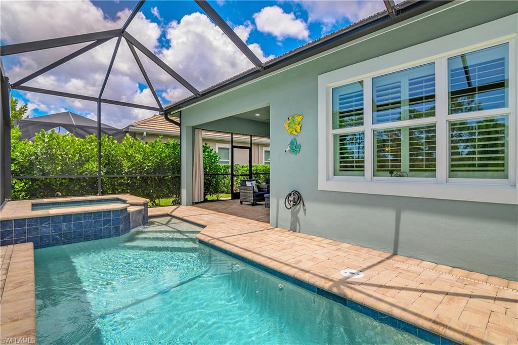 Screened outdoor area featuring a swimming pool, integrated spa with blue tile, and brick paver decking