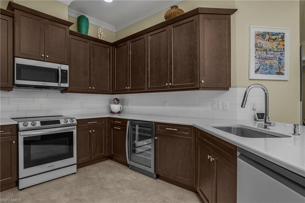 Kitchen featuring dark wood-finish cabinetry, stainless steel appliances, a tile backsplash, light-toned countertops, and a built-in beverage cooler