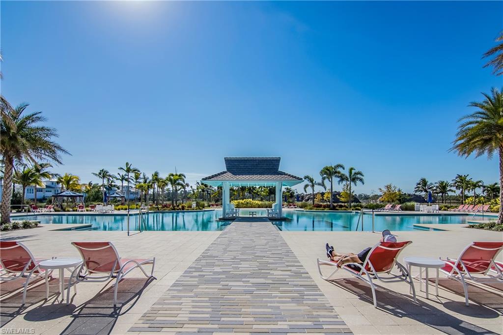 Expansive outdoor pool with a central gazebo structure, surrounded by palm trees and a paved walkway