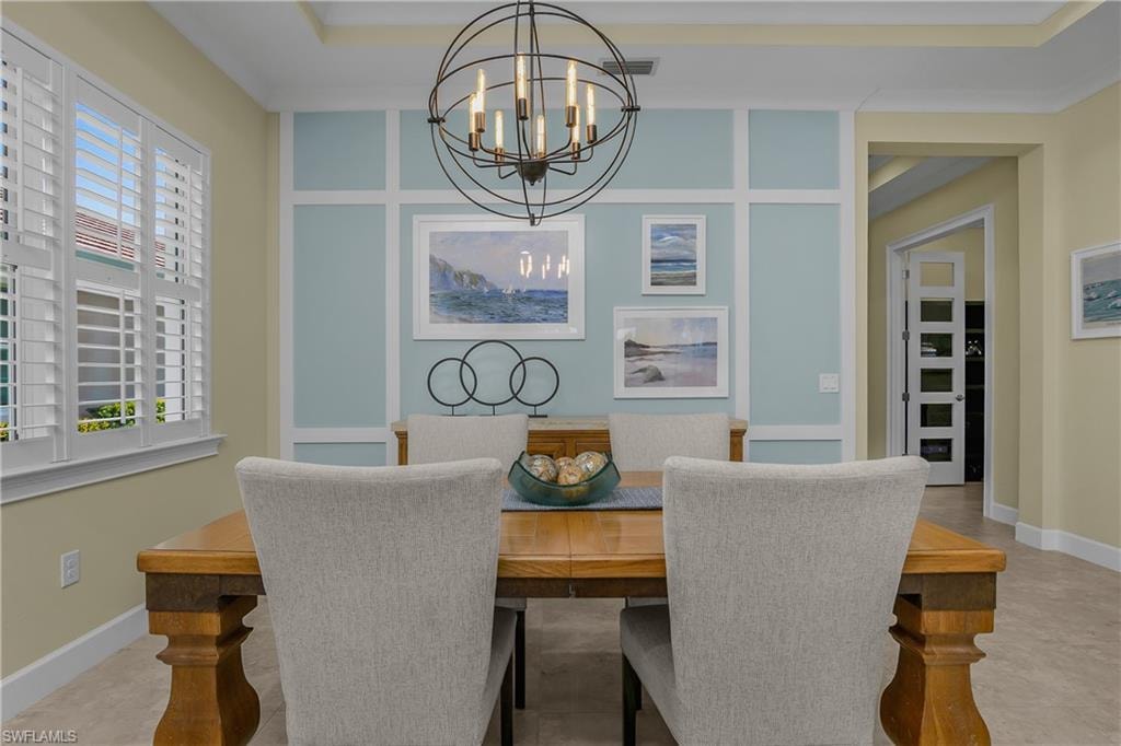 Decorative wainscoting accent wall, overhead spherical chandelier, plantation shutters, tray ceiling, and tile flooring