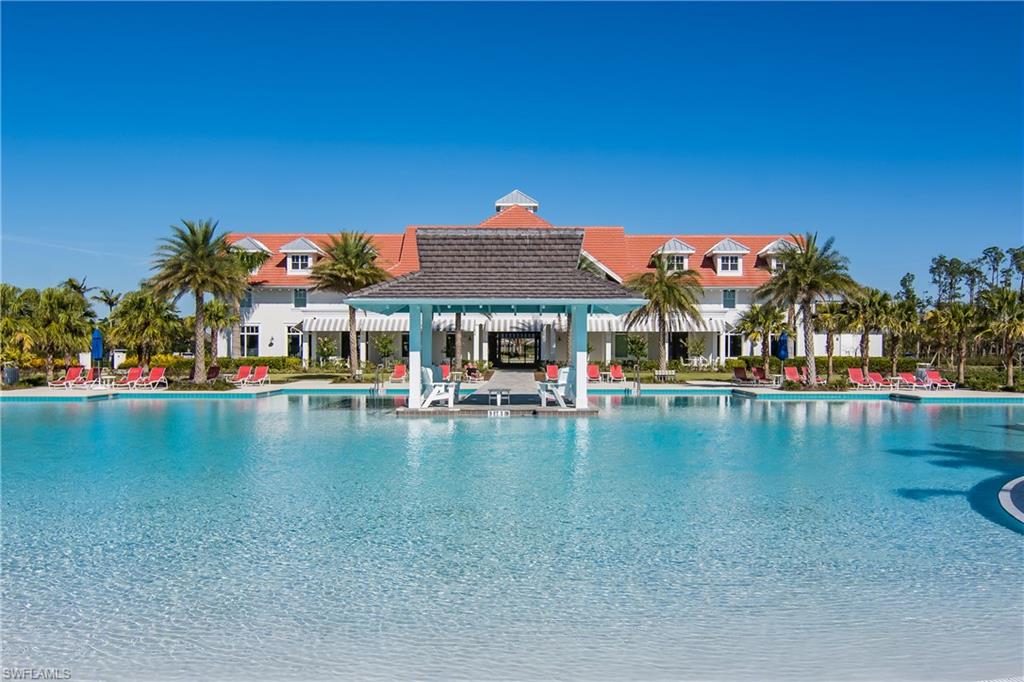 Expansive resort-style pool with a central gazebo, surrounded by palm trees and a white multi-story building featuring a red tile roof and dormer windows