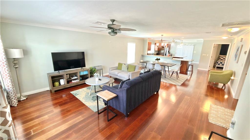 Open-concept living area featuring wood-finish flooring, a ceiling fan, crown molding, and recessed lighting.