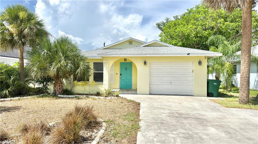 Exterior featuring a vibrant turquoise entry door, arched entryway, an attached garage, and mature palm trees.