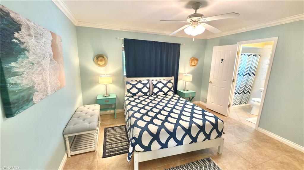Ceiling fan with integrated lighting, crown molding, tile flooring, and a solid door leading to an adjacent bathroom.