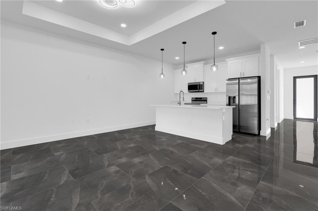 Kitchen with stainless steel appliances, a center island with sink, white cabinets, hanging light fixtures, and open floor plan